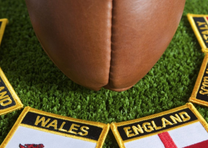 A rugby ball resting on the ground with six embroidered patches for each of the six nations rugby teams