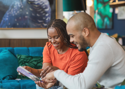 A man and a woman sat on a sofa looking at a CSSC membership leaflet