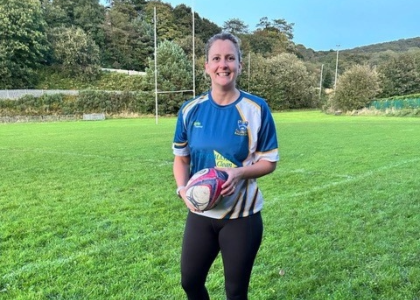 Aimee holding a rugby ball on a rugby pitch
