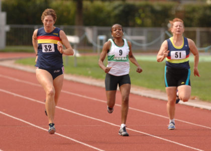 three women running in a race on an athletics track
