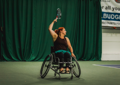 Caroline holding a tennis racket and leaning backwards in her wheelchair