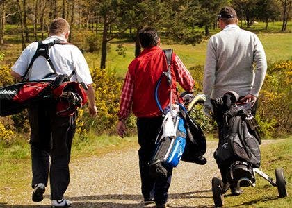 Three golf players making their way to the tee with caddys in tow