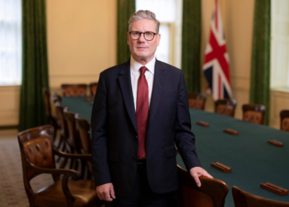 Keir Starmer stood in front of a long green table with chairs and a union jack flag in the background.