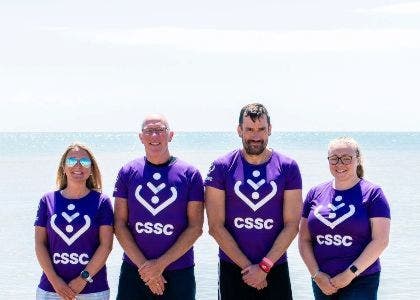 four people in cssc t shirts in front of a beach